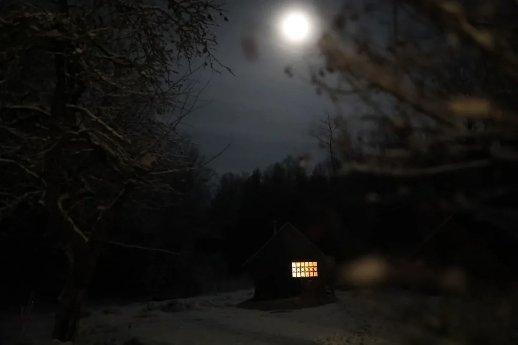 Maison isolée en forêt, une fenêtre éclairée sous la pleine lune